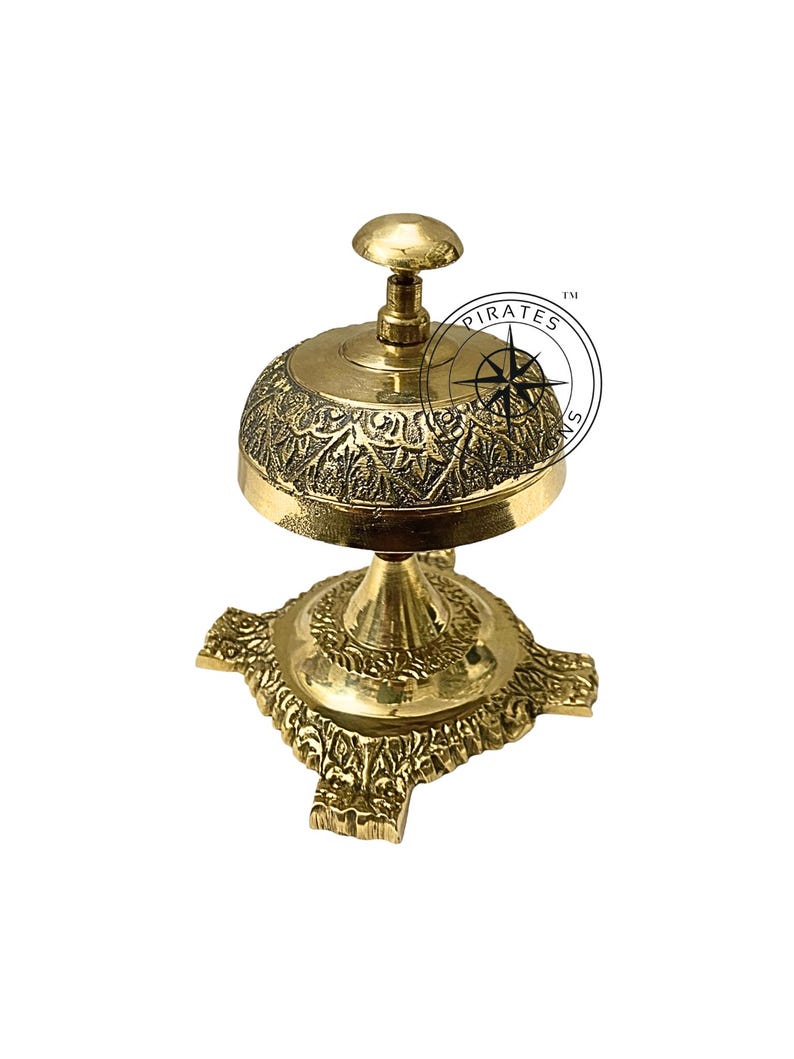 May include: A gold-toned brass service bell with an ornate design. The bell has a round top with a knob and a base with four decorative feet. The bell is engraved with a floral pattern.