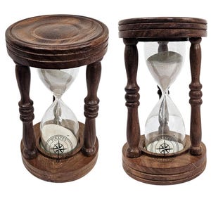Puede incluir: Dos relojes de arena de madera con acabado marrón oscuro. Los relojes de arena tienen un centro de vidrio transparente lleno de arena blanca. La base de cada reloj de arena tiene un diseño de rosa de los vientos con la palabra "PIRATES".