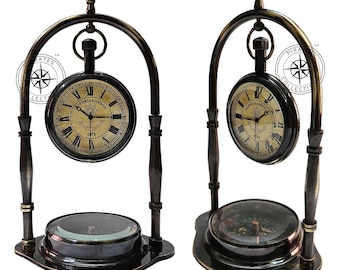 May include: Two antique brass clock stands with a compass base. Each stand features a round clock with Roman numerals and an anchor design. The clocks are suspended from a curved brass arch.