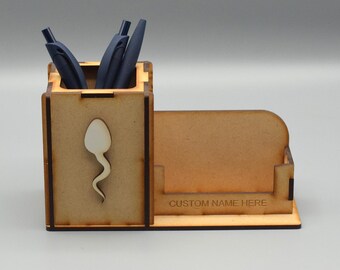 May include: A wooden desk organizer with a pen holder and a business card holder. The pen holder has several blue pens inside. The organizer features a sperm cell design and the text "CUSTOM NAME HERE".
