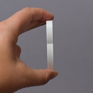 May include: A white, rectangular, adhesive tape dispenser with a brown string attached to it.