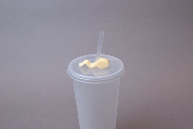 Puede incluir: Un vaso de pl&aacute;stico transparente con tapa y una pajita. La tapa tiene un remolino de glaseado blanco en la parte superior.