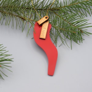 Könnte beinhalten: Ein roter, wellenförmiger Weihnachtsbaumschmuck mit zwei Holzanhängern. Die Anhänger sind mit dem Text "YOUR NAME" und "STEPH" graviert.