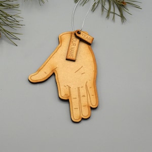 Könnte beinhalten: Weihnachtsbaumschmuck aus Holz in Form einer Hand mit zwei Anhängern. Die Anhänger sind mit "YOUR NAME" und "YEAR" graviert.