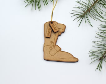 May include: Wooden Christmas ornament shaped like a ski boot with a brown finish. The ornament has two tags attached to it, one that says "YEAR" and the other that says "YOUR NAME".