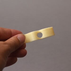Puede incluir: Un solo palito de queso blanco roto con un agujero en el medio. El palito de queso se sostiene en la mano de una persona.