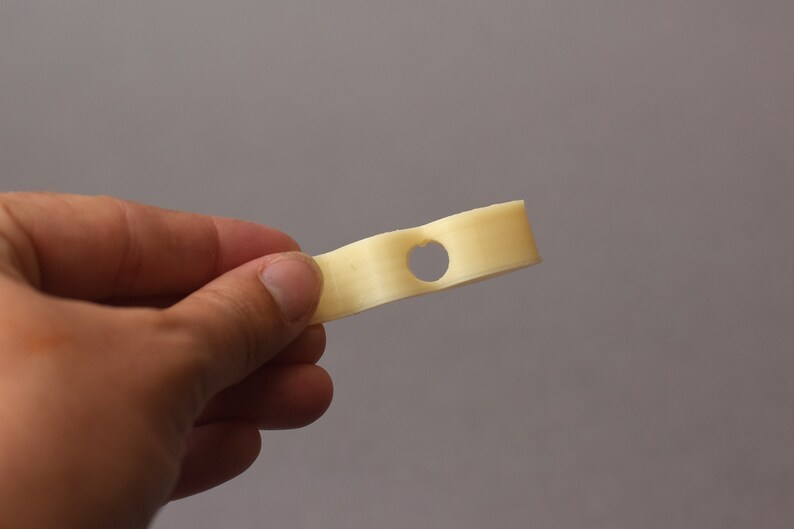 Puede incluir: Un solo palito de queso blanco roto con un agujero en el medio. El palito de queso se sostiene en la mano de una persona.