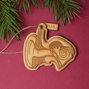 May include: A wooden ornament shaped like a human ear, with the internal structures visible. The ornament is brown and has a string attached for hanging. A small wooden tag with the word "YEAR" is attached to the ornament.