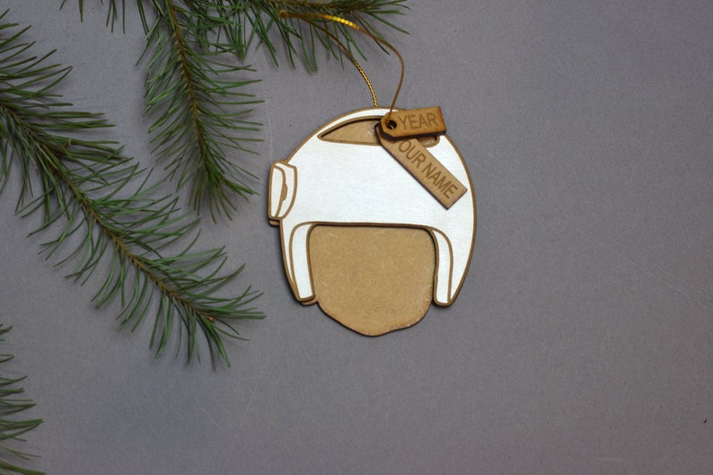 Pu&ograve; includere: Addobbo natalizio in legno bianco e marrone a forma di casco con un'etichetta marrone che dice "YEAR OUR NAME".