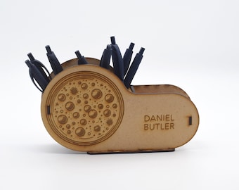 May include: Wooden desk organizer with a circular design featuring a pattern of bubbles and stars. The organizer has a slot for pens and pencils and is engraved with the name "Daniel Butler".