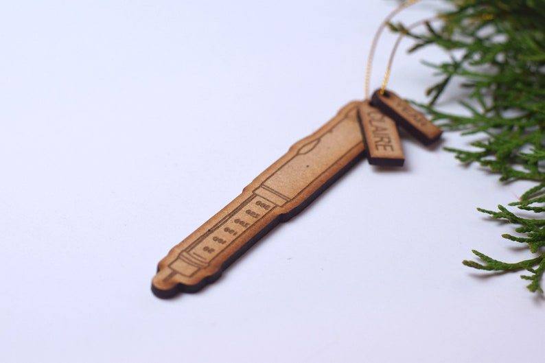 May include: A wooden ornament shaped like a syringe with a tag that reads "CLAIRE".