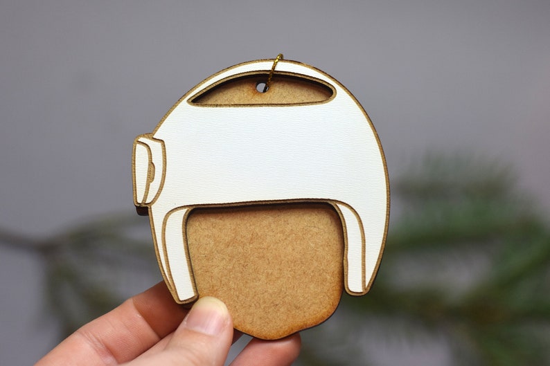 Pu&ograve; includere: Addobbo natalizio in legno bianco a forma di casco con un ritaglio per il viso in legno marrone.