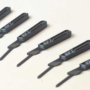 May include: Six black plastic scalpel-shaped tools with a raised inscription that reads "MIFE" on each tool.