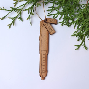 May include: A wooden ornament shaped like a pen with a tag that says "Claire" and another tag that says "Year".