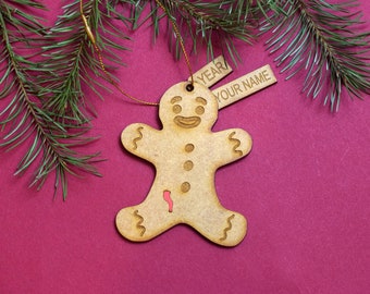 May include: A wooden gingerbread man ornament with a red icing detail. The ornament has a tag that says "YEAR" and "YOUR NAME".