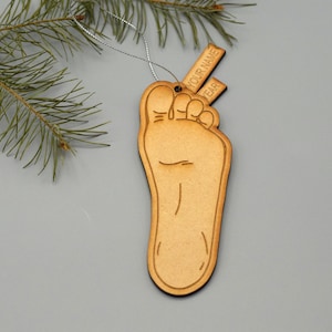 May include: A wooden ornament shaped like a foot with a personalised tag. The tag has the text "YOUR NAME" and "YEAR" on it.