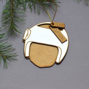 Pu&ograve; includere: Un ornamento natalizio in legno bianco a forma di casco con un'etichetta in legno marrone che dice "YEAR OUR NAME".