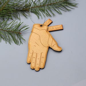 May include: A wooden hand ornament with a cutout design. The ornament has two tags attached to it, one that says "YEAR" and another that says "YOUR NAME".