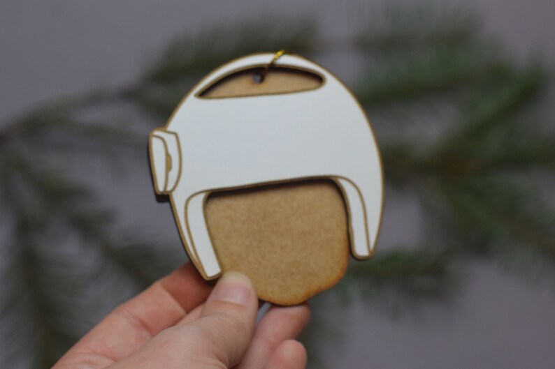 Pu&ograve; includere: Ciondolo in legno bianco a forma di casco con un ritaglio per il viso in legno marrone.