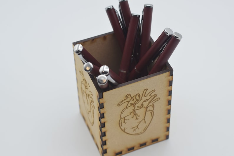 May include: A wooden pen holder with a heart design. The holder is filled with burgundy pens.