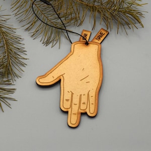 May include: Wooden hand-shaped Christmas ornament with a black string for hanging. The ornament is light brown with a dark brown outline. The word "NAME" is engraved on a small tag. The word "YEAR" is engraved on another small tag.