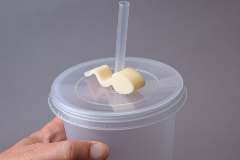 Puede incluir: Un vaso de pl&aacute;stico transparente con tapa y una pajita. La tapa tiene un soporte de pajita de pl&aacute;stico blanco con forma de nota musical.