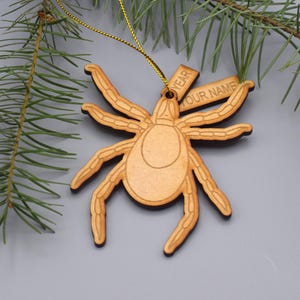 May include: A wooden Christmas ornament shaped like a spider with a tag that says "YEAR YOUR NAME".