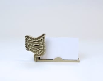 May include: A beige desktop organizer shaped like the human digestive system holds a blank white card.