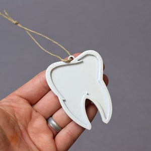 May include: White tooth-shaped ornament with a string loop for hanging. The ornament is made of wood and has a smooth, painted surface.