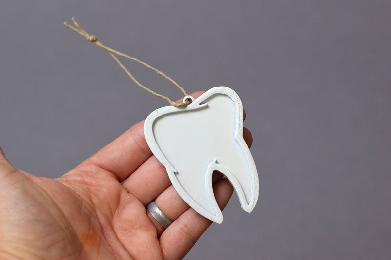 May include: White tooth-shaped ornament with a string loop for hanging. The ornament is made of wood and has a smooth, painted surface.