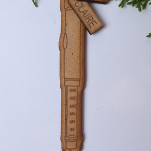 May include: A wooden ornament shaped like a syringe with a scale on the side. The ornament has two tags attached to it, one that says "YEAR" and another that says "CLAIRE".