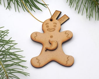 May include: A wooden gingerbread man Christmas ornament with a cutout stomach and a smiling face. The ornament has two blank tags for personalization, one labeled "NAME" and the other "YEAR".
