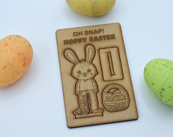 May include: Wooden craft kit featuring a bunny with the text "Oh Snap! Hoppy Easter". The kit includes a bunny, a basket, and a sign. The bunny is holding a basket of eggs. The kit is made of wood and is ready to be assembled.