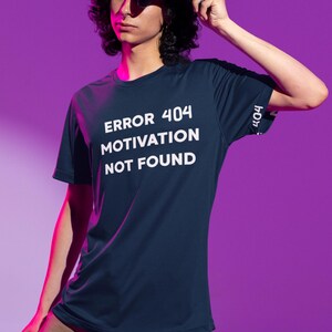 Peut inclure: Un t-shirt bleu foncé à manches courtes avec le texte blanc "ERROR 404 MOTIVATION NOT FOUND" imprimé sur la poitrine. La manche affiche également le nombre "404" en blanc. Le t-shirt est en tissu lisse et possède un col rond.