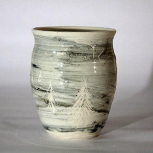 Pode incluir: Um vaso de cerâmica com formato cilíndrico, apresentando um design marmorizado branco e cinza. O vaso tem uma cena de inverno pintada à mão com árvores brancas. O vaso tem cerca de 18 cm de altura.