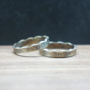 May include: Two gold-toned rings made from Hong Kong coins. The top ring has the text "HONG KONG" and the year "1961" inscribed on it. The bottom ring has the text "HONG KONG" inscribed on it.