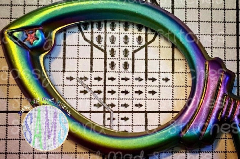 May include: A close-up of a rainbow-colored metal hoop with a star design. The hoop is on a gridded surface with arrows pointing to the right. The text "Cross Stitch" is visible on the surface.