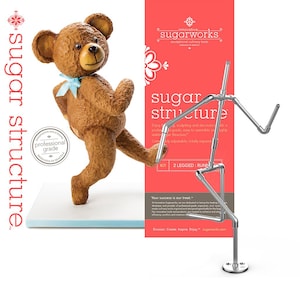 May include: A silver metal sugar structure kit in the shape of a running person. The kit is made of pipes and connectors. The kit is on a white surface with a brown teddy bear in the background. The text on the packaging reads "sugar structure" and "innovative sugarworks".