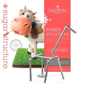 May include: A silver metal sugar structure kit for building, sculpting, and decorating cakes. The kit includes a base, four legs, and a long arm. The kit is shown assembled with a model of a cow made of fondant on top. The text on the image reads "sugar structure" and "innovative sugarworks exceptional culinary tools".