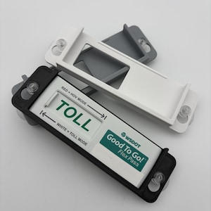 May include: A black and white plastic holder for a WSDOT Good To Go! Flex Pass. The black holder contains a white pass with green text reading TOLL, RED = HOV MODE, and WHITE = TOLL MODE. Two additional empty holders in white and gray are stacked behind.