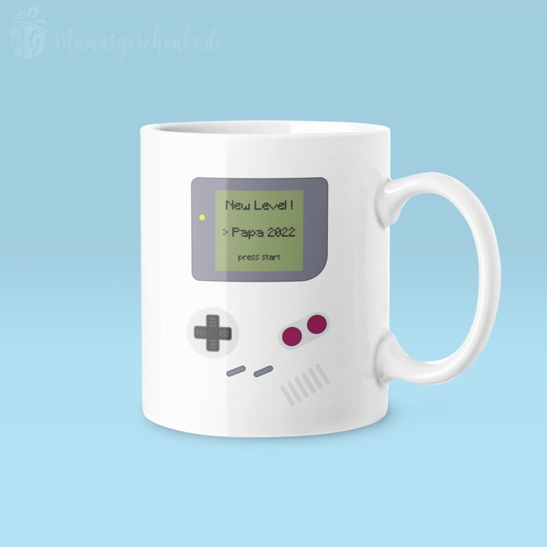 Puede incluir: Taza de cer&aacute;mica blanca con una ilustraci&oacute;n gris y verde de una consola de videojuegos retro con el texto "New Level! > Papa 2022 press start".