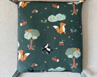 Puede incluir: Cesta de tela cuadrada con un diseño de bosque sobre un fondo verde oscuro. El patrón presenta zorros naranjas, erizos y tejones entre árboles, troncos y setas. Tiene cuatro pestañas en las esquinas para colgar.