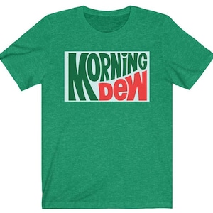 May include: Green t-shirt with the text "MORNING DEW" in a rectangular design. The text is in a mix of green, red, and white colors. The shirt is made of a soft material.