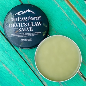 May include: A round, dark teal tin of Devil's Claw Salve from Four Peaks Soapery, with a white rim and a light green salve inside. The tin lid features white text and a mountain graphic. The net weight is 4 oz (113 gr).