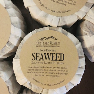 May include: A bar of handmade soap with a brown paper label that reads "Seaweed Soap with Cactus & Tallow". The label also includes the ingredients, "distilled water, pureed cactus paddle, saponified oils (olive oil, coconut oil, beef tallow, castor oil), organic kelp powder, bentonite clay. Unscented." The label also states "Four Peaks Soapery, Hand Cut, All Natural Cold Process Soaps, Cold Process, Net Weight 4-5 oz, Made in the Southwest".