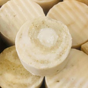 May include: Close-up of a stack of round, white soap bars with a swirl pattern. The soap bars have a light brown color and a textured surface.