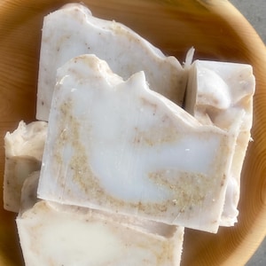 May include: Three bars of handmade soap with a white base and brown swirls. The soap is in a wooden bowl.