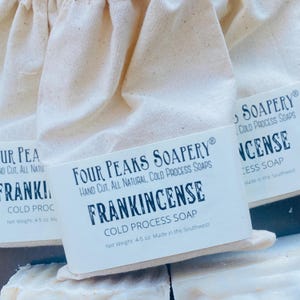 May include: Close-up of three bars of Frankincense cold process soap, each wrapped in a natural fabric bag. The soap bars are labeled with the brand "Four Peaks Soapery" and the text "Frankincense Cold Process Soap". Each bar weighs 128-142 grams.
