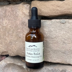 May include: A brown glass bottle with a black dropper top. The bottle is labeled "Four Peaks Soapery" and "Gotu Kola Herbal Healing Oil". The label also states "Net Weight: 1 oz. (29.57 ml)".
