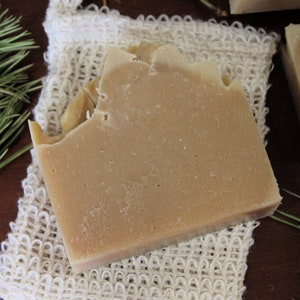 May include: A light brown bar of soap resting on a white crocheted soap saver.